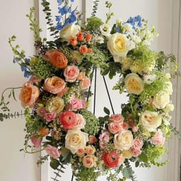 Large floral wreath with roses, ranunculus, and blue delphinium on a stand
