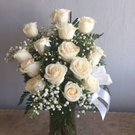 Cream rose bouquet in a clear glass vase with baby's breath and a white ribbon