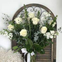 White roses and white filler flowers in a glass vase with greenery
