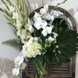 White orchids and gladiolus arranged in a clear glass vase