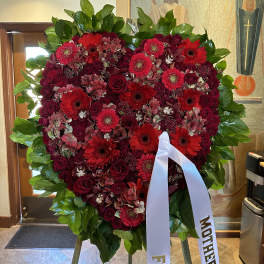 Heart-shaped red floral wreath on an easel with white ribbons