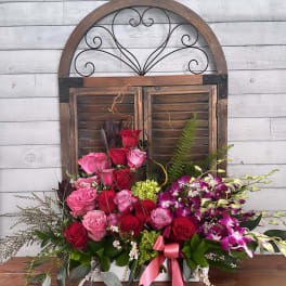 Mixed pink and red roses with purple orchids in a white container