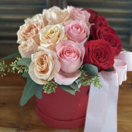 Bouquet of pink, peach, and red roses in a red hat box with a white ribbon