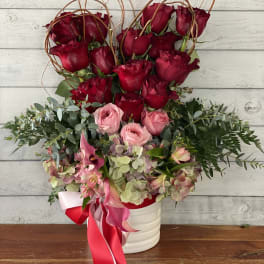 Red roses and pink flowers arranged in a white vase with ribbon