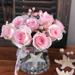 Pink roses arranged in a clear glass vase with a patterned ribbon