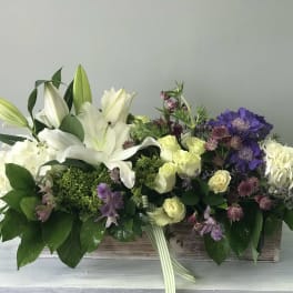 Low floral centerpiece with white lilies, cream roses, and purple blooms in a wooden box