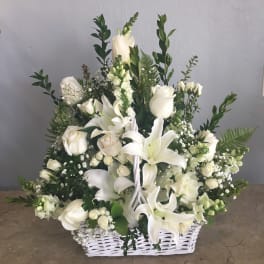 White floral arrangement in a white basket with roses and lilies