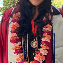 Graduate in maroon cap and gown with a flower lei