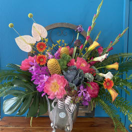 Large tropical floral arrangement in a silver urn with pink, purple, and orange blooms