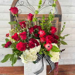 Red roses and white hydrangeas in a white vase with a striped ribbon