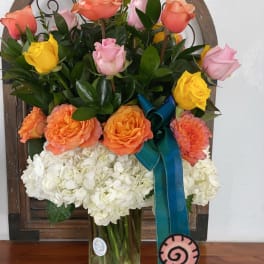 Mixed roses and white hydrangeas in a glass vase with a blue ribbon