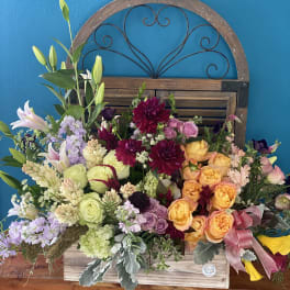 Large mixed flower arrangement in a wooden box with a pink ribbon