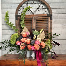 Peach and pink rose arrangement in a metal container with ribbon