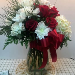 Bouquet of red roses and white flowers in a glass vase with a red ribbon