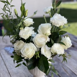 White roses and ruffled white blooms arranged in a white pedestal vase