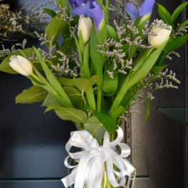 Bouquet of purple and white tulips in a glass vase with a white ribbon