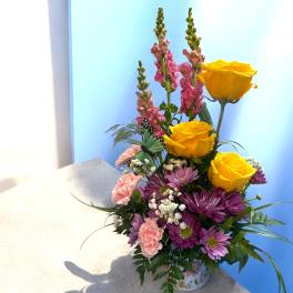 Bouquet of yellow roses, purple daisies, and pink snapdragons in a floral container