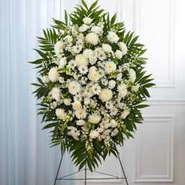 Standing spray of white roses, daisies, and mums with palm fronds on a metal easel.