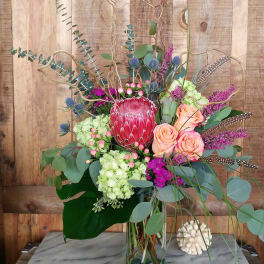 Tall mixed bouquet with a red protea and peach roses in a glass vase