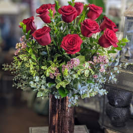 Red roses arranged in a tall copper vase with mixed greenery