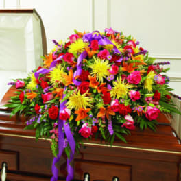 Colorful floral casket spray with purple ribbon on a wooden casket
