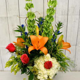 Tall mixed bouquet with orange lilies, red roses, and white hydrangeas in a glass vase