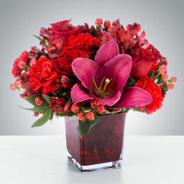 Red floral arrangement in a square glass vase with a pink lily centerpiece