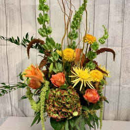 Tall mixed floral arrangement in a glass vase with orange and yellow blooms