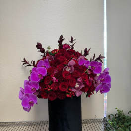 Red rose and purple orchid arrangement in a black cylinder vase