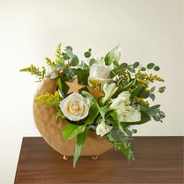 White roses and lilies in a gold crescent vase with greenery