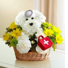 White flower teddy bear in a wicker basket with yellow flowers and a red first-aid bag