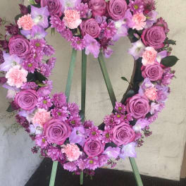 Heart-shaped floral wreath with pink roses and purple flowers on a stand