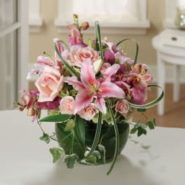 Pink lilies and roses arranged in a green glass vase
