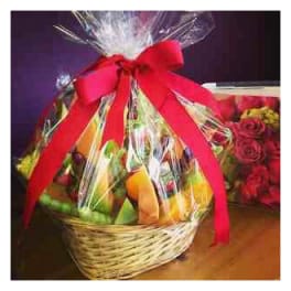 Gift basket with fruit and flowers wrapped in clear cellophane and a red bow
