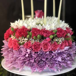 Tiered floral cake with pink, white, and purple flowers and tall candles