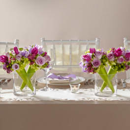 Two pink and lavender floral centerpieces in clear glass vases on a set table