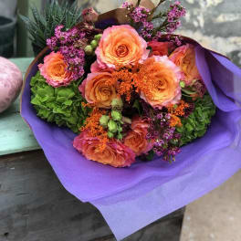 Bouquet of peach roses and purple filler flowers wrapped in lavender paper