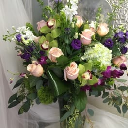 Tall bouquet of pink roses, purple orchids, and white blooms in a glass vase
