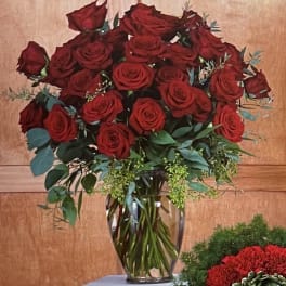 Red roses arranged in a clear glass vase with greenery