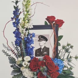 Floral tribute around a framed black-and-white portrait with red roses and blue-white flowers