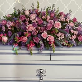 Large pink and purple floral spray on a white casket