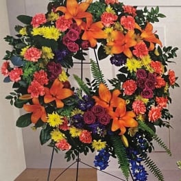 Large floral wreath with orange lilies, pink roses, and yellow and coral blooms