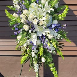 Tall funeral spray of white lilies, roses, and blue flowers on a stand
