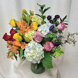 Mixed bouquet of roses, hydrangeas, lilies and other blooms in a clear glass vase