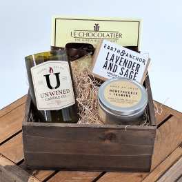 Gift basket with a candle, soap, chocolate, and a tin container in a wooden crate