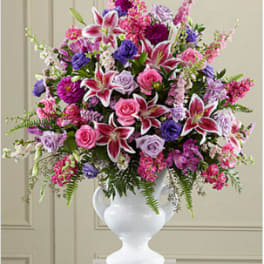 Tall arrangement of pink lilies, roses, and purple flowers in a white urn vase