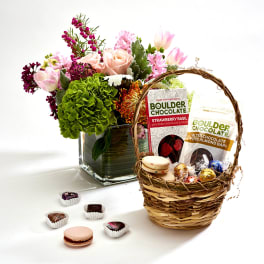 Flower arrangement in a glass vase beside a basket of chocolates and macarons