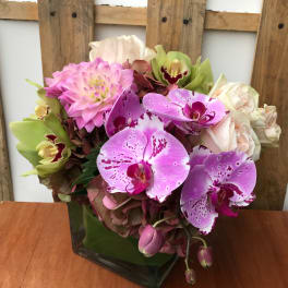 Pink and purple orchid arrangement in a square glass vase