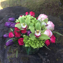 Bouquet of pink roses, purple tulips, and green orchids in a glass vase