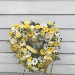 Heart-shaped wreath of white and yellow flowers with a yellow ribbon